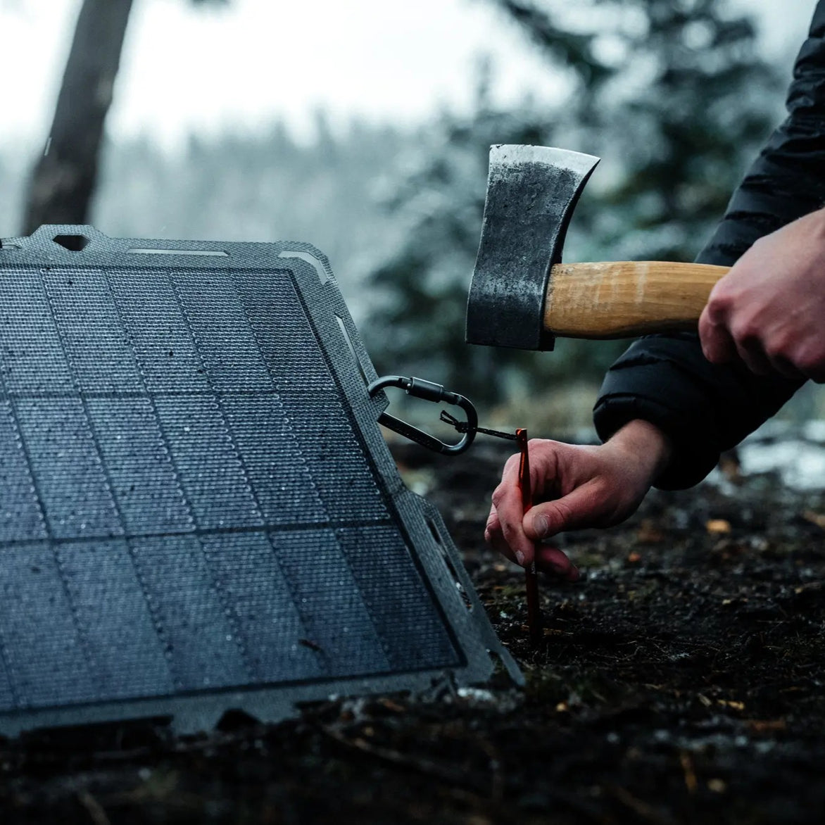 A person staking the Spectre solar panel to the ground with a hatchet.