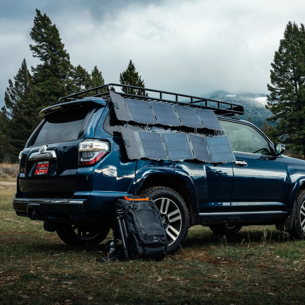 The Spectre 56W solar panel laid across the roof of an SUV at a campsite.