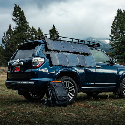 The Spectre 56W solar panel laid across the roof of an SUV at a campsite.