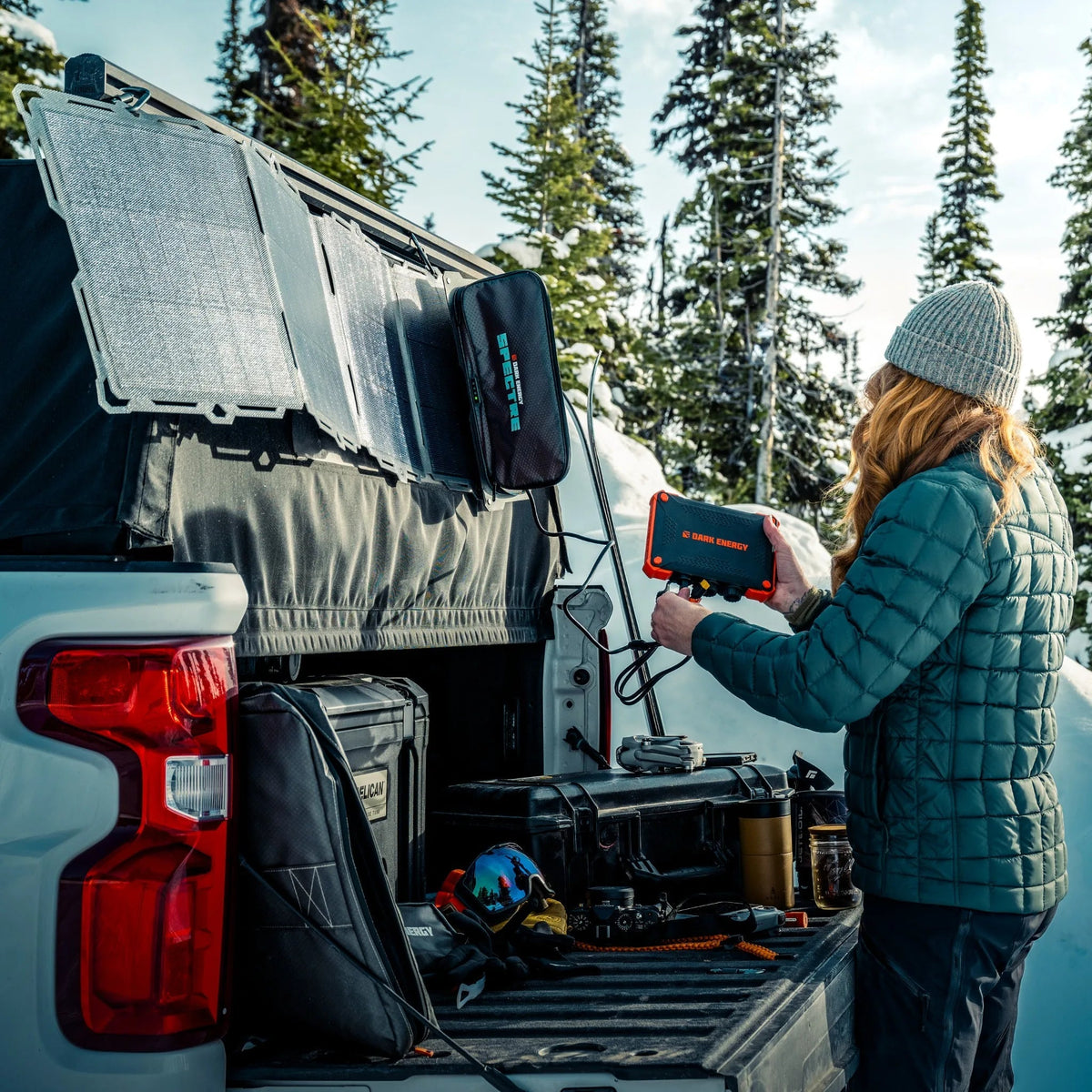 A woman using a Dark Energy power bank at the back of a truck in snow.