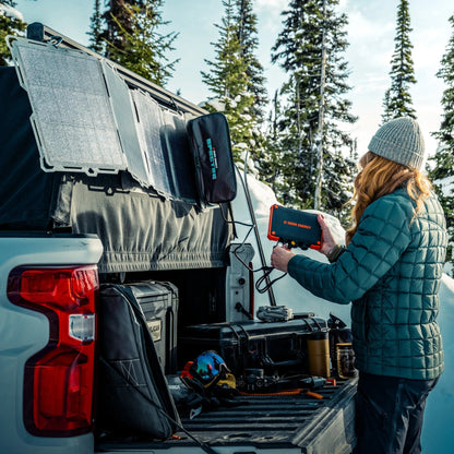 A woman using a Dark Energy power bank at the back of a truck in snow.